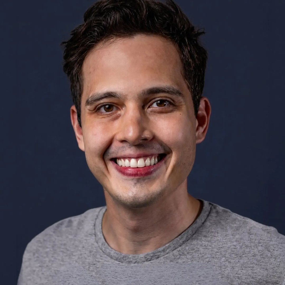 Renato Tamaoki sorrindo, de camiseta cinza, em fundo azul-escuro